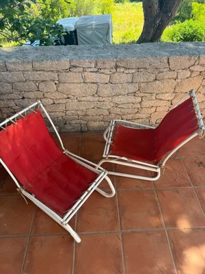 two red lawn chairs sitting on a patio near a stone wall