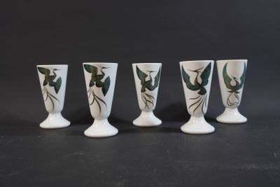 four white vases with green leaves on them sitting on a black surface