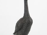 a small metal duck that is standing on a white surface