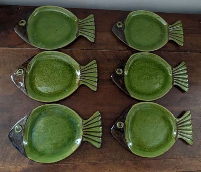 six green fish shaped dishes sitting on a wooden table
