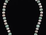 a necklace made of white pearls and green jade beads on a black background