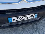 the front end of a white car with a number plate on it