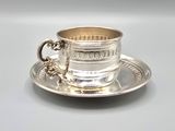 a silver cup and saucer sitting on a saucer