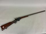 un fusil avec un canon en bois et une crosse en métal, posé sur une surface blanche