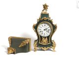 une horloge verte et dorée posée à côté d'un livre