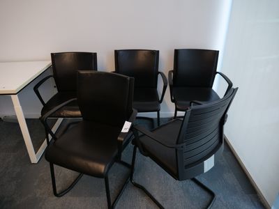 Trois chaises noires sont posées dans un coin, près d'une table blanche.