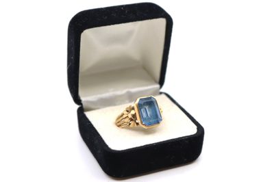 une photo d'une bague en or sertie d'une pierre bleue, dans un écrin noir