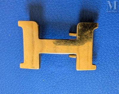 a gold metal letter h on a blue leather surface