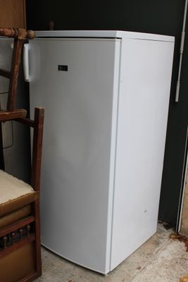 un réfrigérateur blanc posé à côté d'une chaise dans une pièce