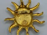a close up of a gold sun brooch on a white surface