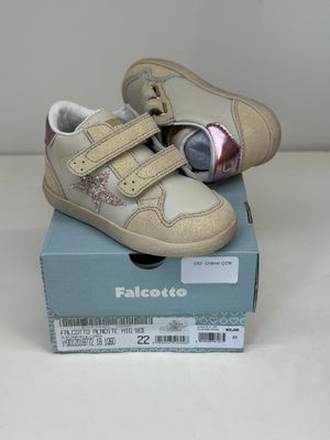 des chaussures de bébé beiges et roses dans une boîte posée sur une surface blanche