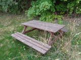 a wooden picnic table in the middle of a grassy area