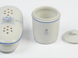 un vase blanc orné d'une fleur bleue, à côté d'une tasse
