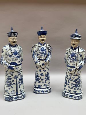 trois figurines bleues et blanches représentant des hommes coiffés d'un chapeau et vêtus d'une redingote
