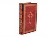 an old red book with a cross on it sitting on top of a white surface