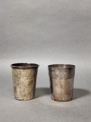 two silver cups with designs on them sitting on a table