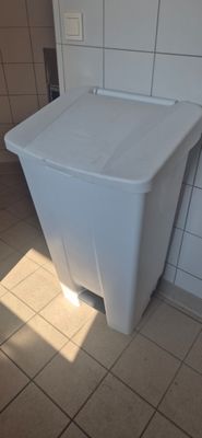 a white trash can sitting on the floor in a bathroom