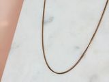 un collier à chaîne en or posé sur une surface en marbre