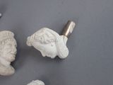 three white sculptures of heads and a pipe on a gray surface