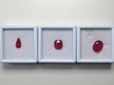 trois pierres précieuses rouges se trouvent dans une boîte blanche posée sur une surface blanche