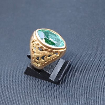 une image représentant une bague en or sertie d'une pierre verte, posée sur un socle
