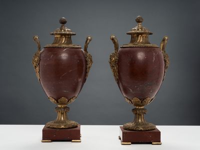 une paire de vases anciens munis d'anses, posés sur des socles, sur un fond blanc
