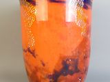 un vase orange posé sur une table, sur fond gris