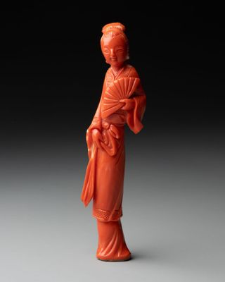 une figurine en jade orange représentant une femme tenant un éventail