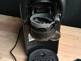 a black coffee maker on a wooden table with a charger