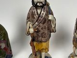 three ceramic figurines of asian men and a bell on a white surface