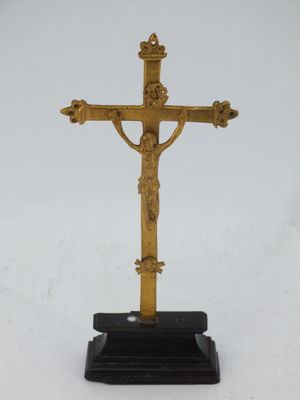 une croix dorée posée sur un socle noir, sur fond blanc