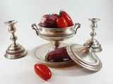 a bowl of vegetables on a silver plate next to two silver candlesticks
