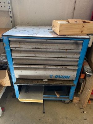 une armoire à outils bleue posée dans un garage, à côté d'un tas de bois