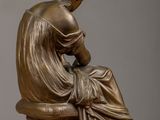 bronze statue of a woman sitting on a chair with her hands on her knees