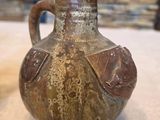 a brown vase sitting on a table with a stone wall in the background