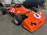 an orange race car parked in a garage next to a black car