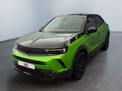 La voiture verte est garée dans une grande pièce au sol noir.