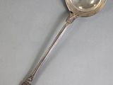 an antique silver spoon with a spoon handle on a gray surface