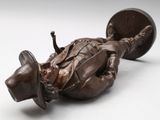 a statue of a man laying on the ground next to a coin
