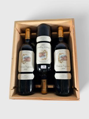 trois bouteilles de vin se trouvent dans une caisse en bois posée sur une surface blanche