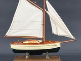 maquette en bois d'un voilier aux voiles blanches, posée sur un socle en bois