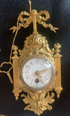 a gold clock hanging on the wall with a chain