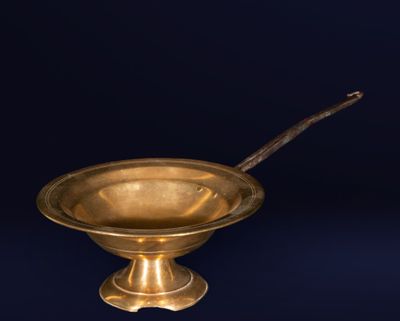 un bol ancien en laiton avec une cuillère, sur fond bleu