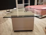une table en verre au milieu d'une pièce, avec un lit en arrière-plan
