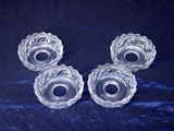 four clear glass candlestick holders on a blue background