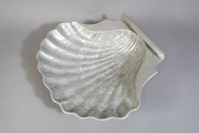 un plat argenté en forme de coquillage posé sur un fond blanc