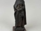 une statue représentant une femme vêtue d'une cape, posée sur un socle en bois