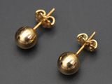 une paire de boucles d'oreilles en forme de boules dorées posées sur une surface noire