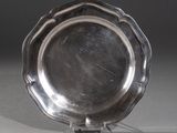 un plat ancien en argent posé sur un support, sur fond gris