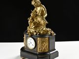 a clock that is sitting on a table with a statue on top of it